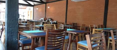 Un comedor interior con mesas y sillas de madera, paredes de ladrillo y una estructura de techo de madera.