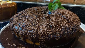 A chocolate cake with sprinkles on a white plate, surrounded by sliced salami and a loaf of bread.