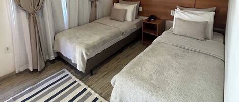 A hotel room with two beds, a striped rug, a nightstand, and a wall-mounted picture.