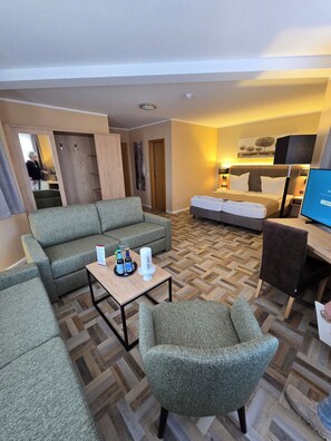 A modern hotel room with a sofa, armchair, and a bed. There is a small table with drinks and a candle. - Landgasthaus Zander (Blankenburg)