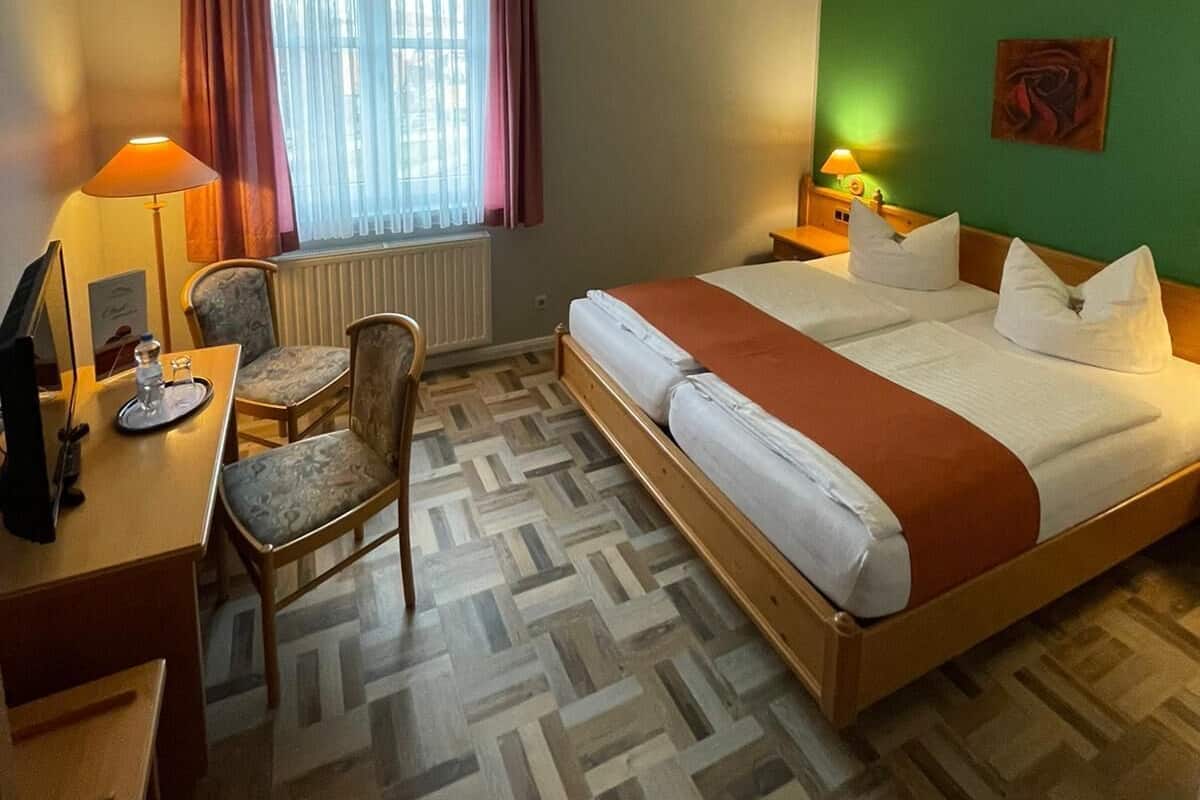 A hotel room with a bed, a desk, a chair, a lamp, and a painting on the wall.