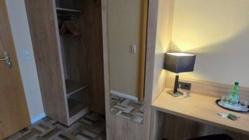 Ein Hotelzimmer mit einem Holzschrank, einem Schreibtisch mit Lampe, einem Stuhl und einem Fiskgrätparkettboden.