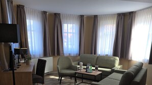 A hotel room with a sofa, armchair, coffee table, desk with a lamp, and a television. - Landgasthaus Zander (Blankenburg)