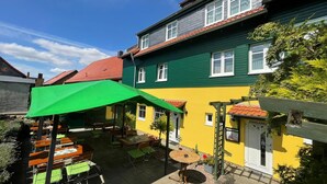 A courtyard with outdoor seating, a green umbrella, and a yellow building with a red roof. - Landgasthaus Zander (Blankenburg)