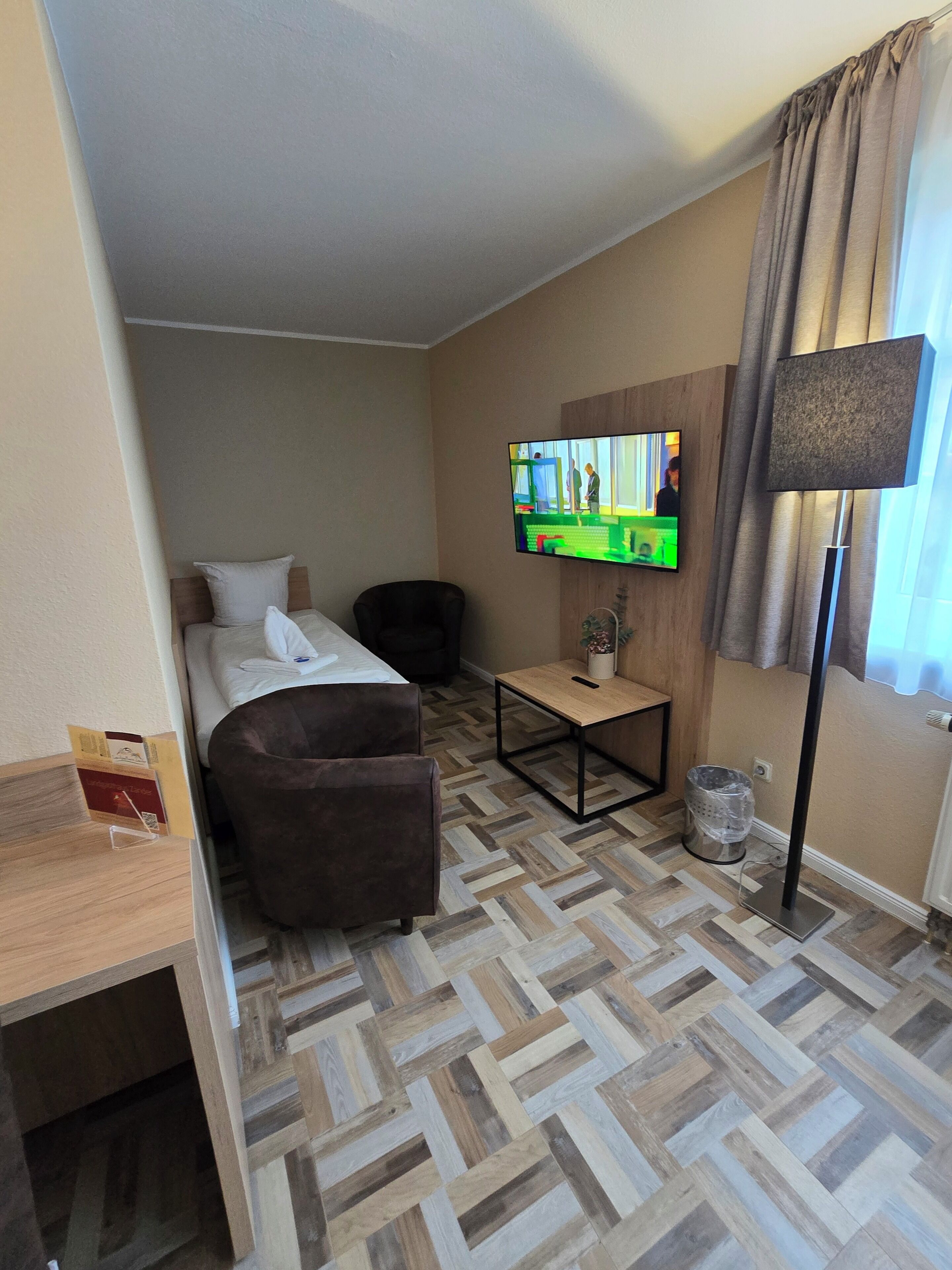 Una camera d'albergo con un letto, due poltrone, una TV a muro, un tavolino e una lampada da terra.