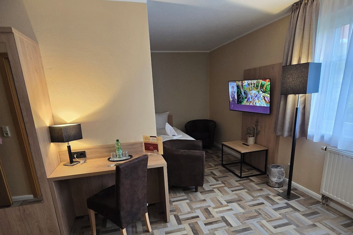 A hotel room with a bed, a desk, a chair, a television, and a floor lamp.