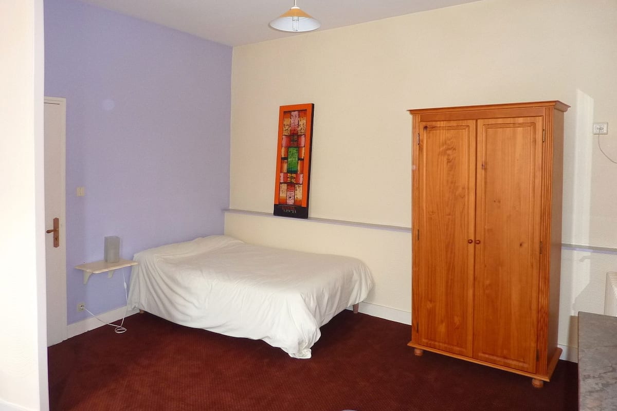 A bedroom with a bed, a wardrobe, a shelf, and a wall-mounted artwork.
