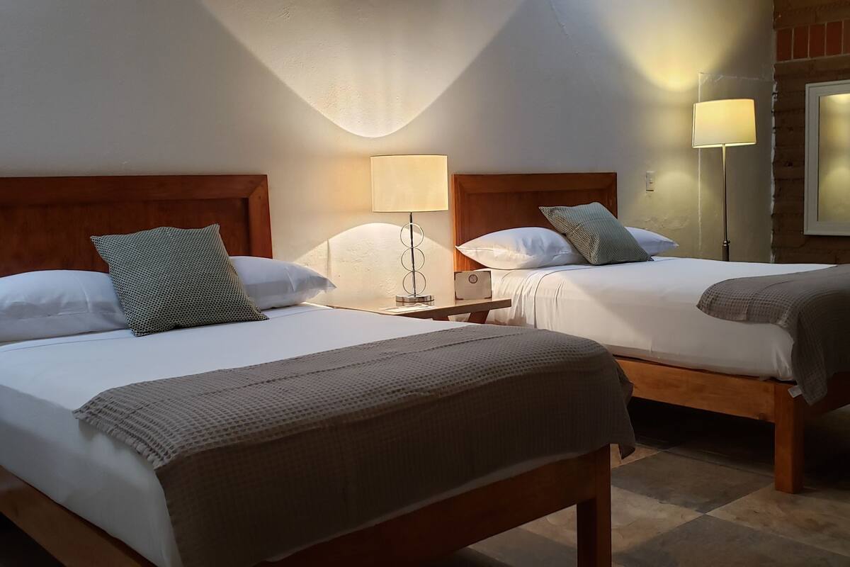 Habitació d'hotel amb dos llits de fusta, llençols blancs i un mirall a la paret.