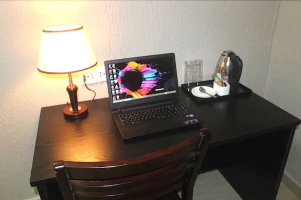 Una computadora portátil sobre un escritorio de madera con una lámpara, una cafetera y una taza de café.
