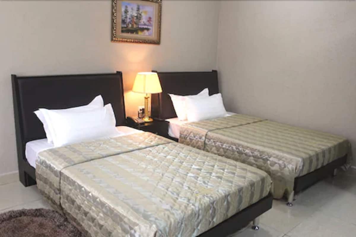 A hotel room with two beds, each with a headboard, a nightstand with a lamp, and a framed picture on the wall.