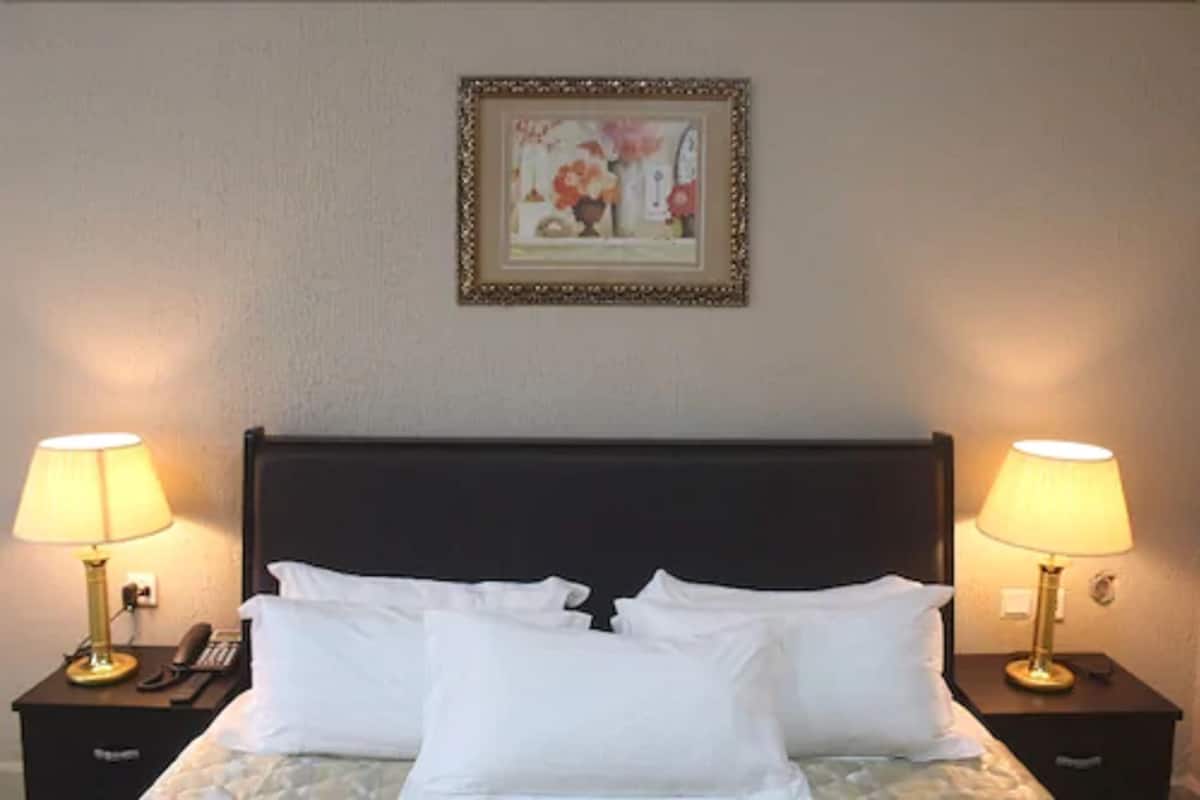A hotel room with a bed, two bedside tables, lamps, a framed picture, and a telephone.