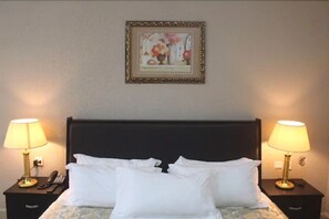 A hotel room with a bed, two bedside tables, lamps, a framed picture, and a telephone. - Corina Hotel (Monrovia)
