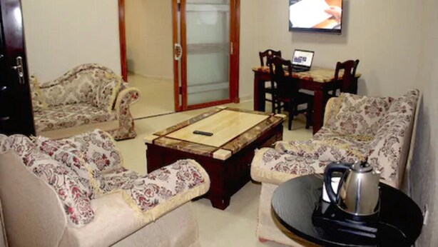 A living room with patterned sofas, a coffee table, a TV, and a laptop on a desk. - Corina Hotel (Monrovia)