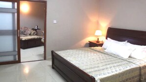 A bedroom with a bed, a nightstand with a lamp, and a bicycle in the background. - Corina Hotel (Monrovia)