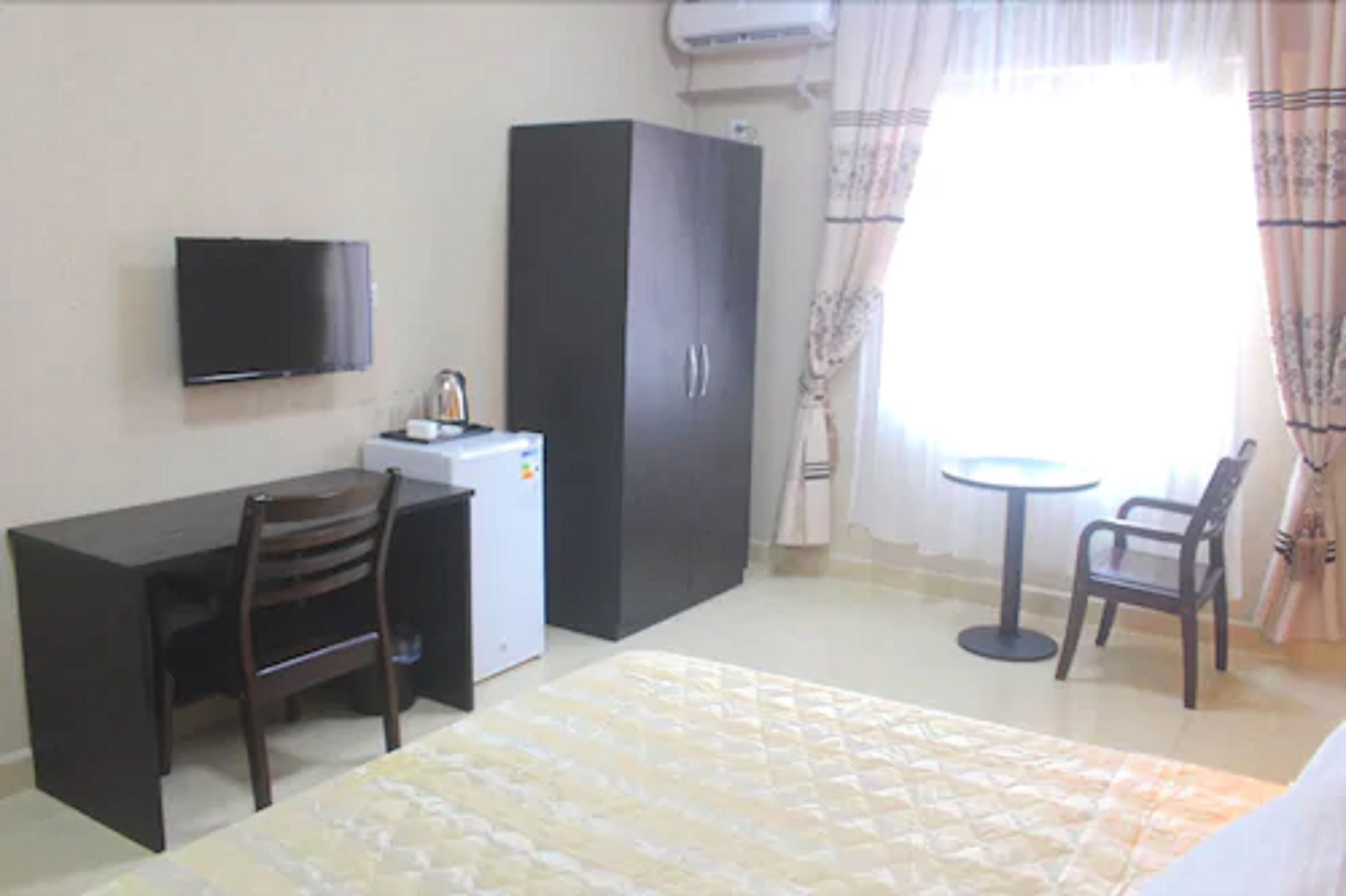 A room with a bed, a desk, a chair, a wardrobe, a television, and a small table with a chair.