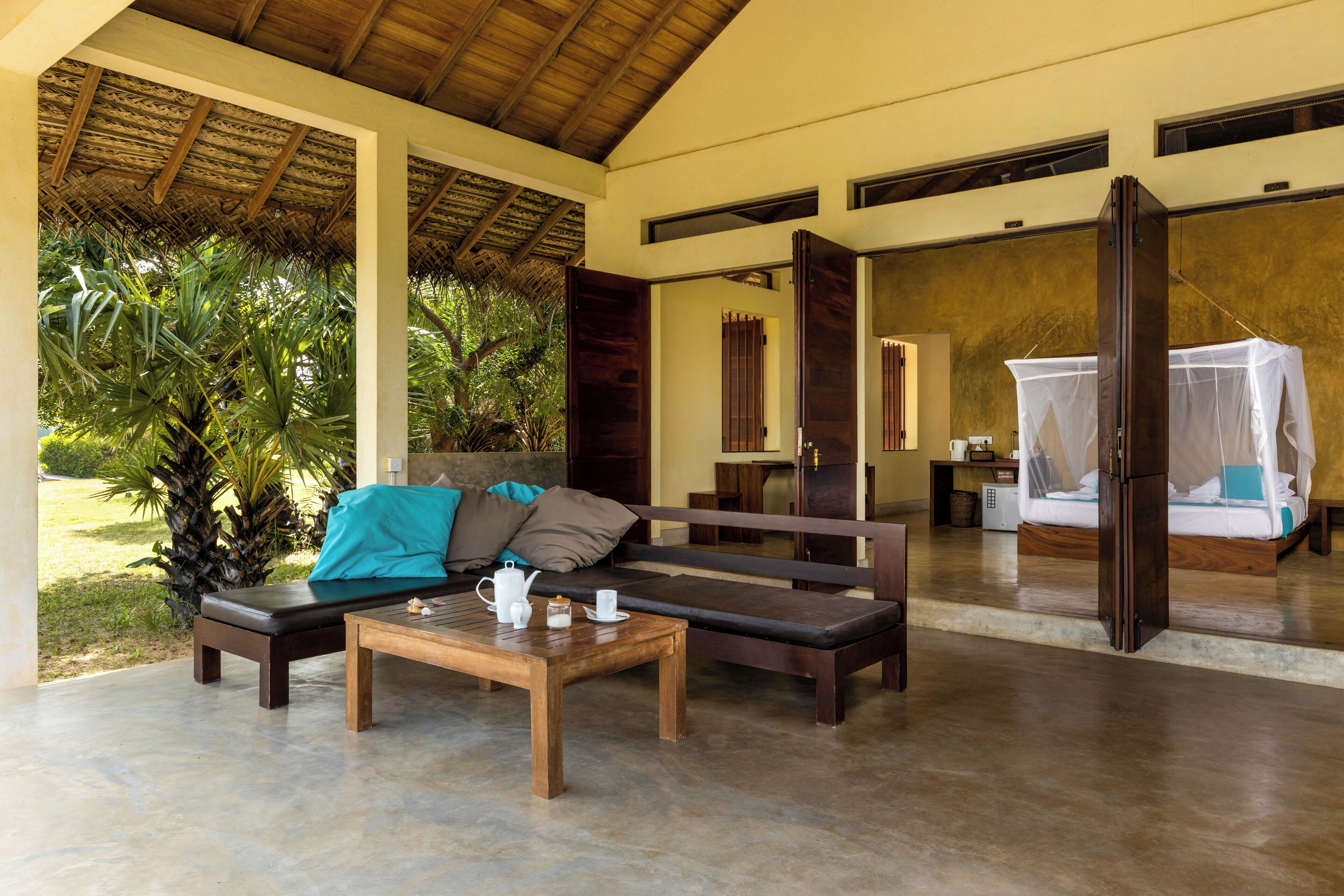 A room with a wooden bench, a table with a teapot and cups, and a bed with a mosquito net.