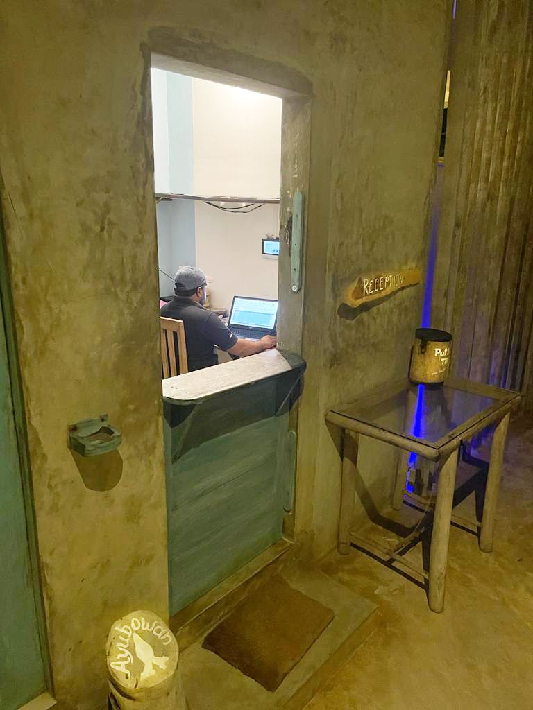 A reception area with a person working at a desk, a reception sign, and a small table with a lamp.