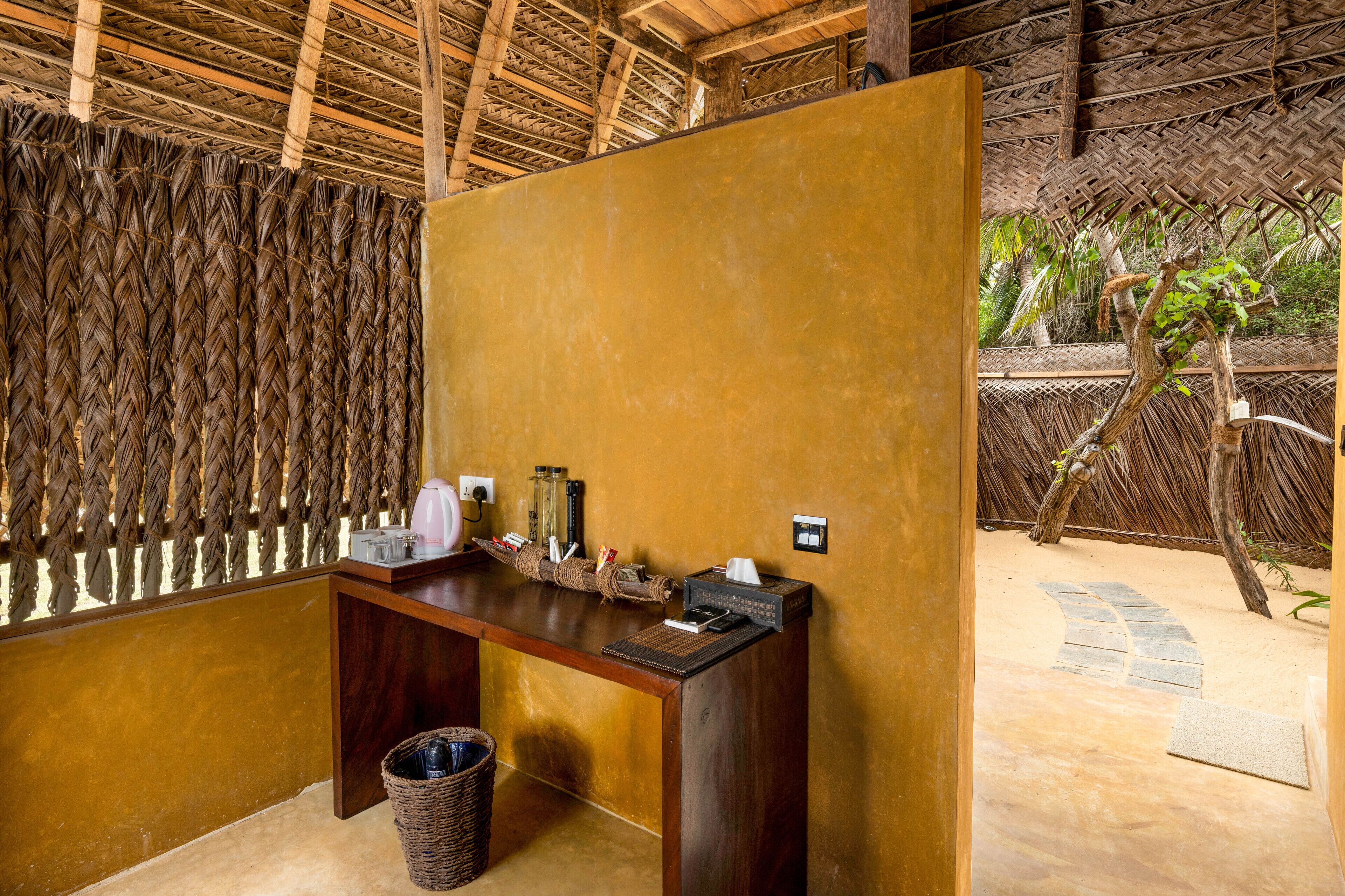 A reception desk with a woven partition, a trash bin, and a stone pathway leading outside.