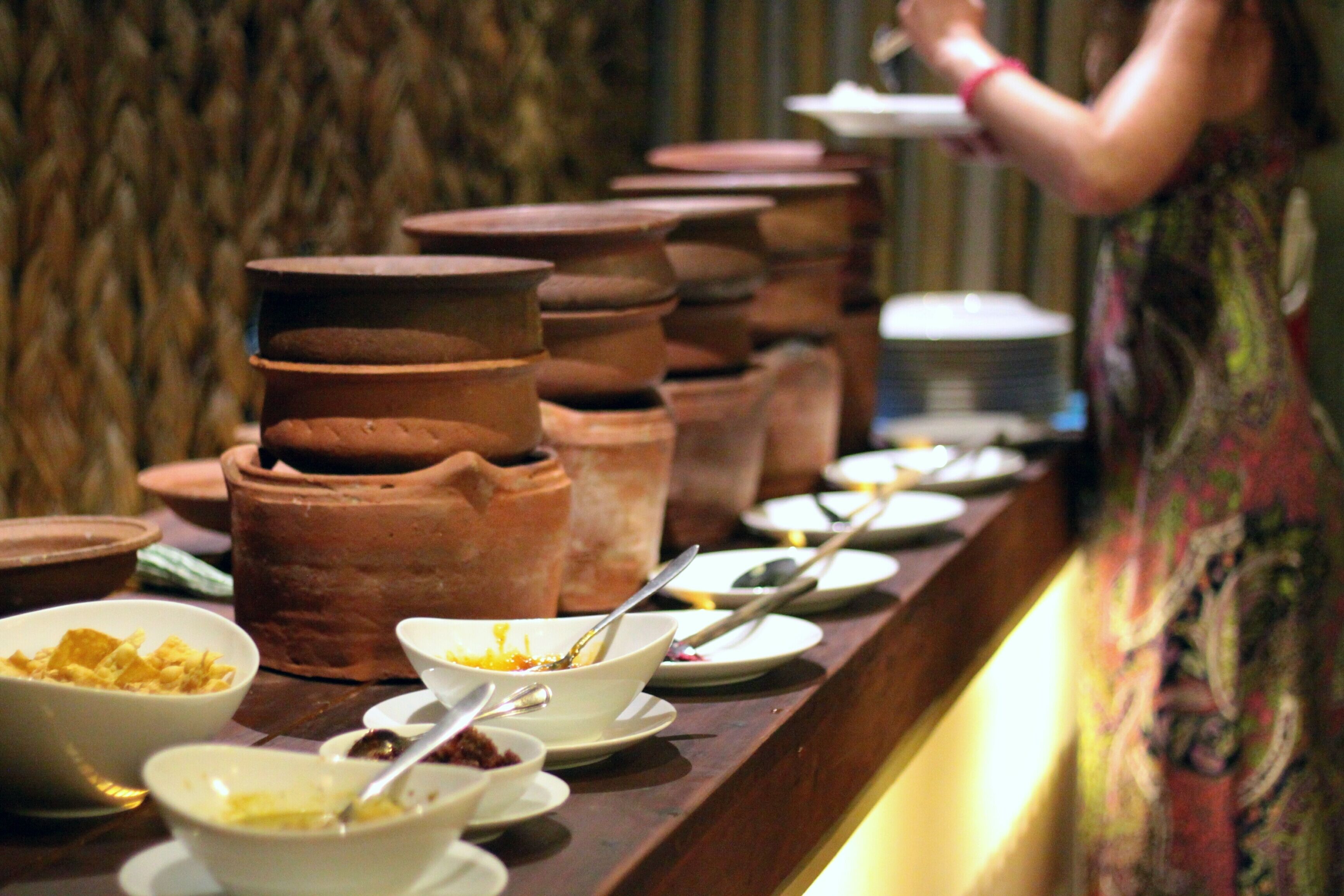 A buffet with various dishes and utensils, including bowls and plates, arranged on a counter.