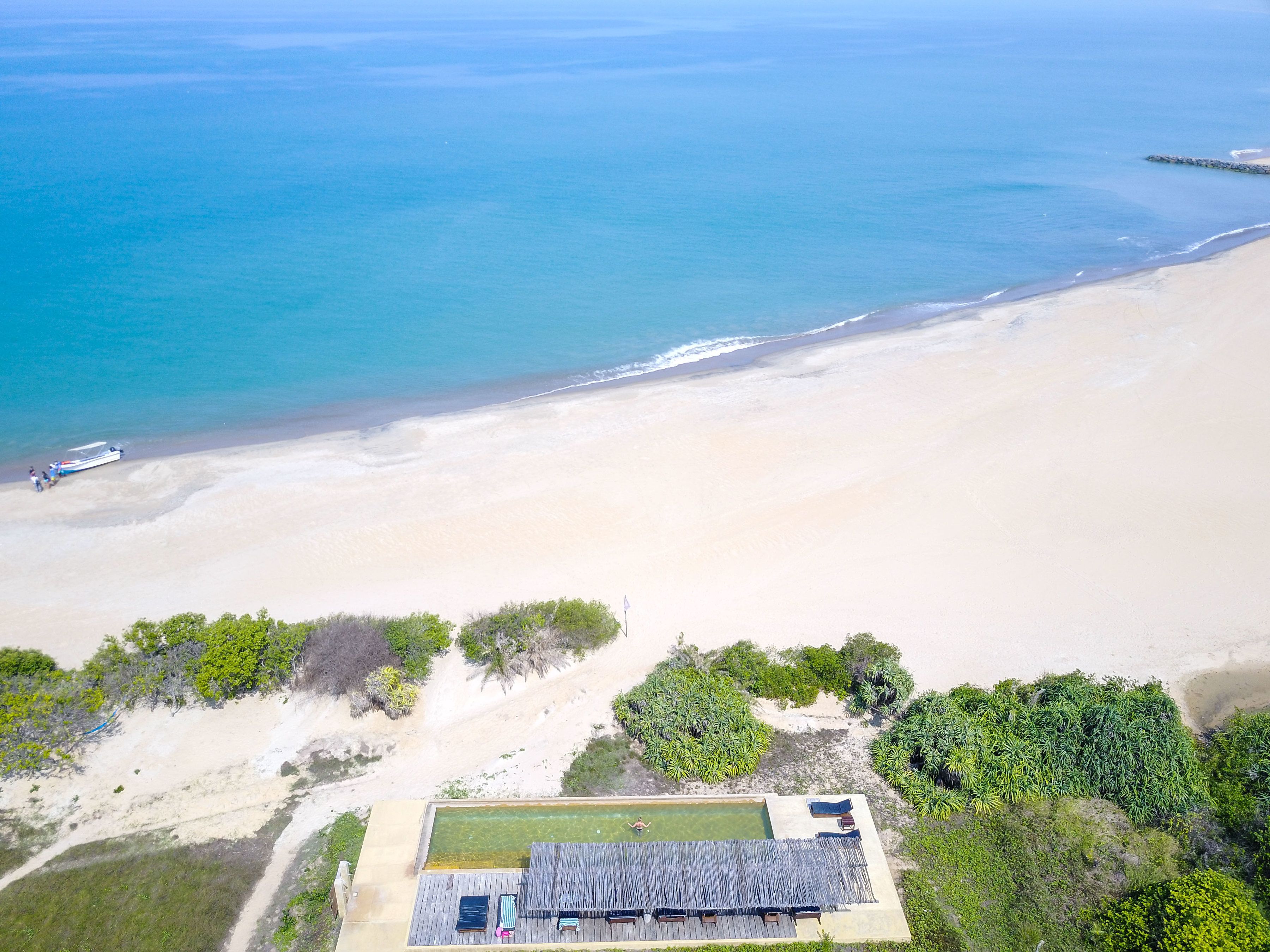Vista aérea de una propiedad frente a la playa, con piscina, terraza de madera y exuberante vegetación.