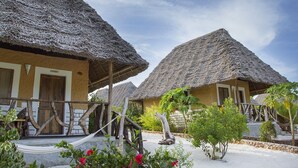 A row of thatched-roof cottages with wooden balconies and a sandy ground. - Ujamaa Beach Resort Zanzibar (Makunduchi)