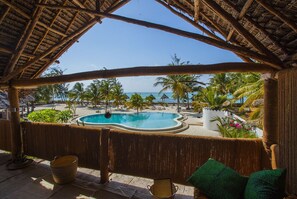 A pool area with a view of the beach and ocean, surrounded by palm trees and a thatched roof structure. - Ujamaa Beach Resort Zanzibar (Makunduchi)