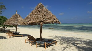 A beach with thatched umbrellas and wooden lounge chairs. - Ujamaa Beach Resort Zanzibar (Makunduchi)