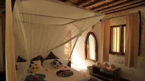 A bed with a canopy, pillows, a bedside table, and a window with curtains. - Ujamaa Beach Resort Zanzibar (Makunduchi)