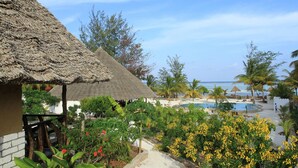 A resort with thatched-roof huts, a pool area, and tropical vegetation. - Ujamaa Beach Resort Zanzibar (Makunduchi)