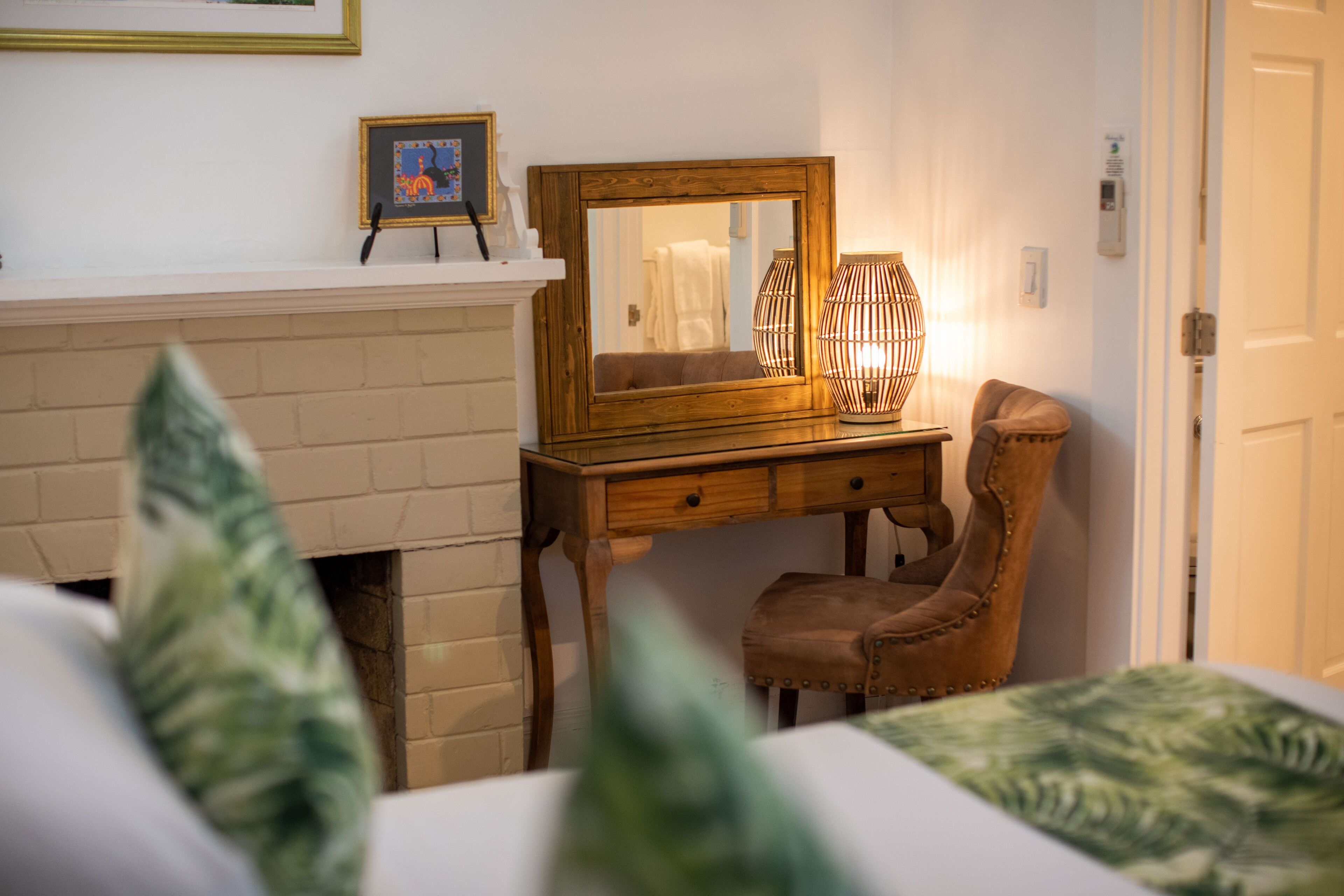 Une chambre à coucher avec une commode en bois, un miroir, une chaise et un lit recouvert d’une literie à motifs verts.