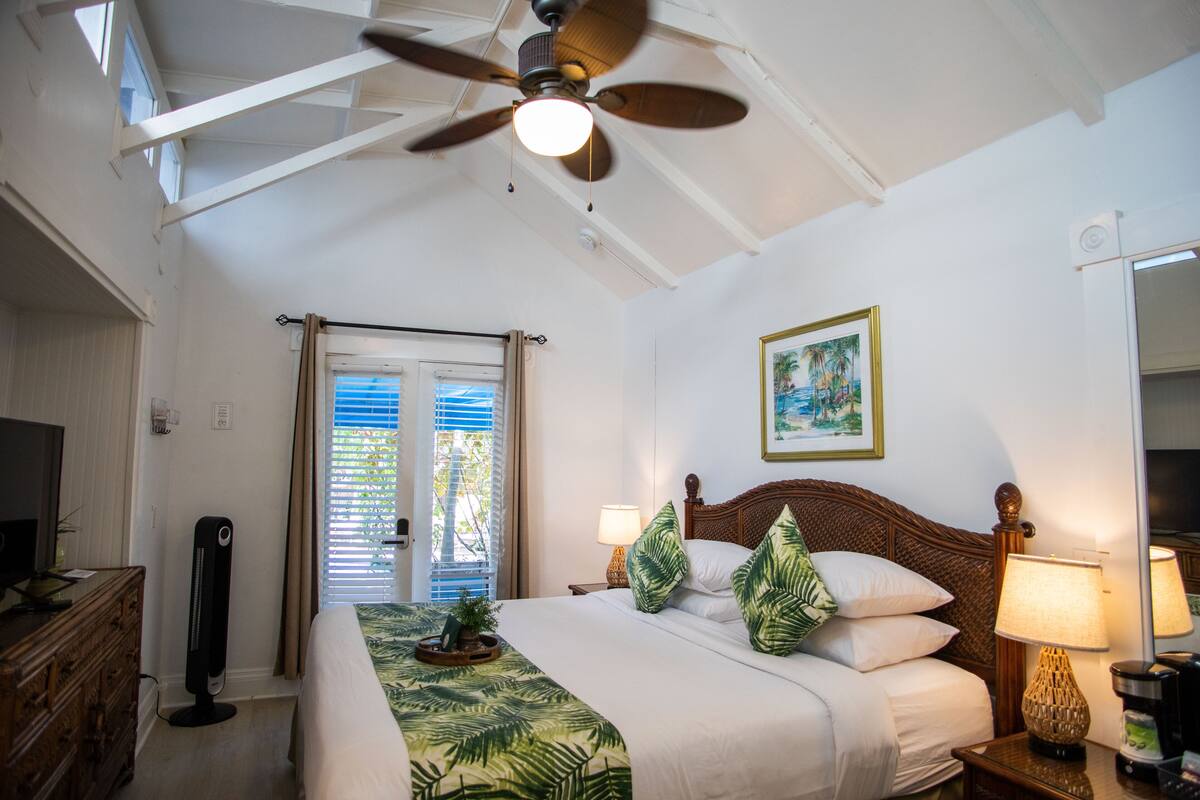 Une chambre d’hôtel équipée d’un lit, d’un ventilateur de plafond, de lampes de chevet et d’une fenêtre avec des stores.