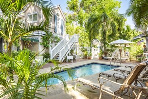 A pool area with lounge chairs, a staircase leading to a house, and lush greenery.