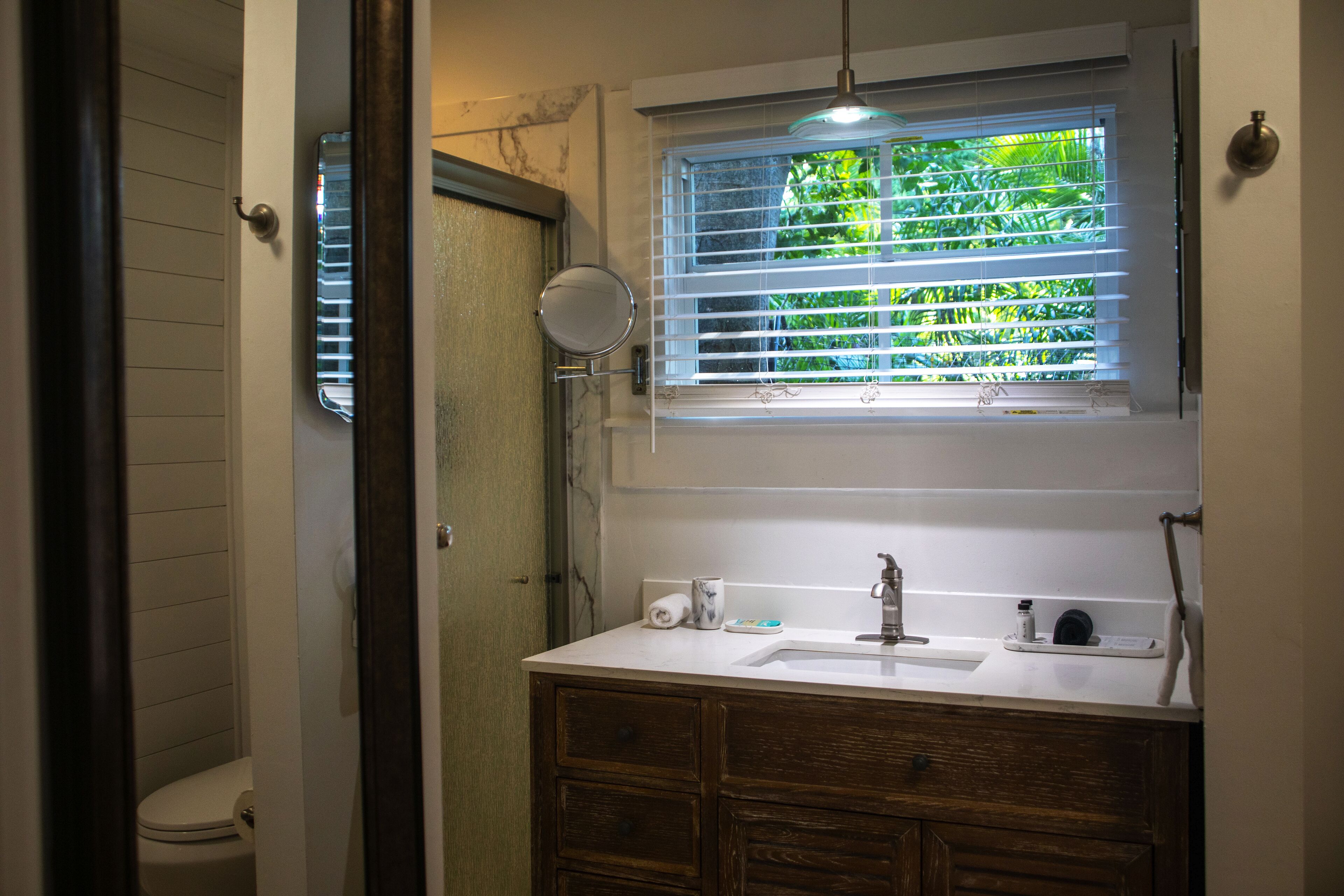 A bathroom with a toilet, a sink with a mirror, and a window with blinds.