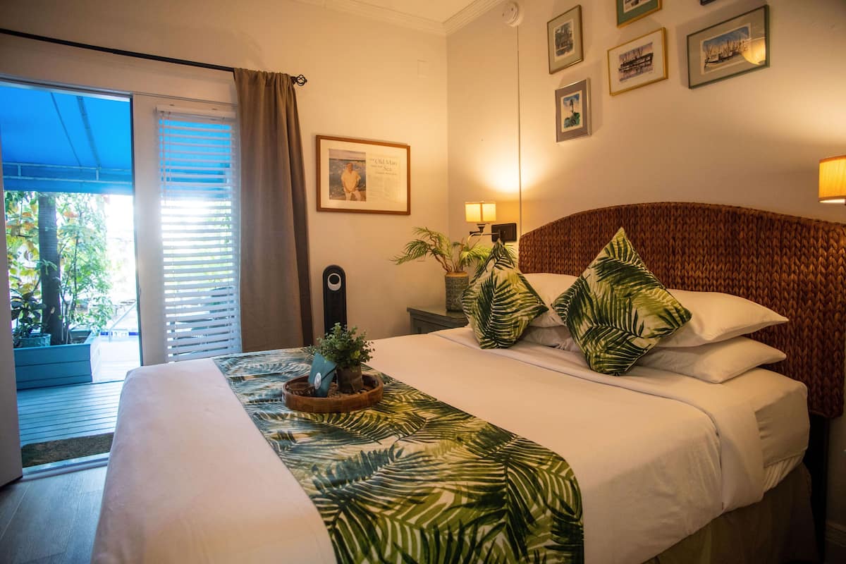 Une chambre d’hôtel avec un lit, une table de chevet avec une lampe, une plante en pot et une vue sur l’extérieur grâce à une porte coulissante.