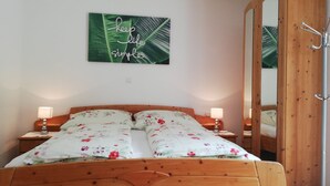 A bedroom with a wooden bed, floral bedding, two bedside lamps, a mirror, and a wall with a 'keep it simple' sign. - Ferienwohnungen Fam. Pabst (Maria Lankowitz)