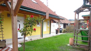 A yellow building with a red-tiled roof, a wooden play structure, and a well-maintained lawn. - Ferienwohnungen Fam. Pabst (Maria Lankowitz)