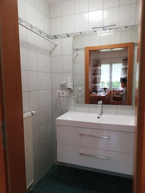 Un baño con azulejos blancos, un lavamanos blanco, un espejo y una zona de ducha.