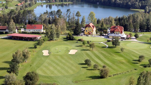 A golf course with sand bunkers, a clubhouse, and a lake in the background. - Ferienwohnungen Fam. Pabst (Maria Lankowitz)