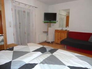 Un dormitorio con una cama, televisor, espejo, sofá rojo y un armario de madera.