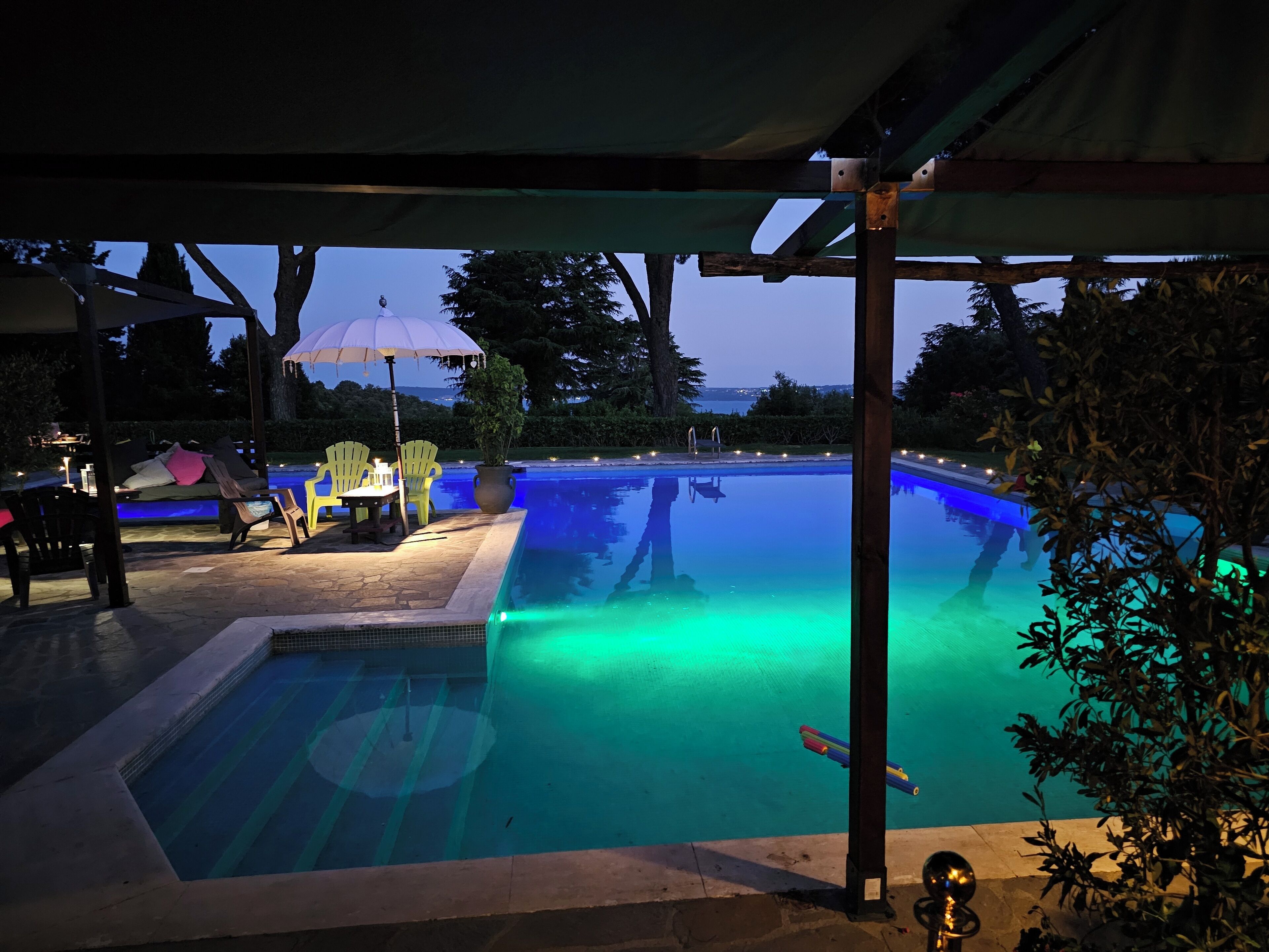 A swimming pool with a view of the ocean, surrounded by outdoor seating and a covered area.