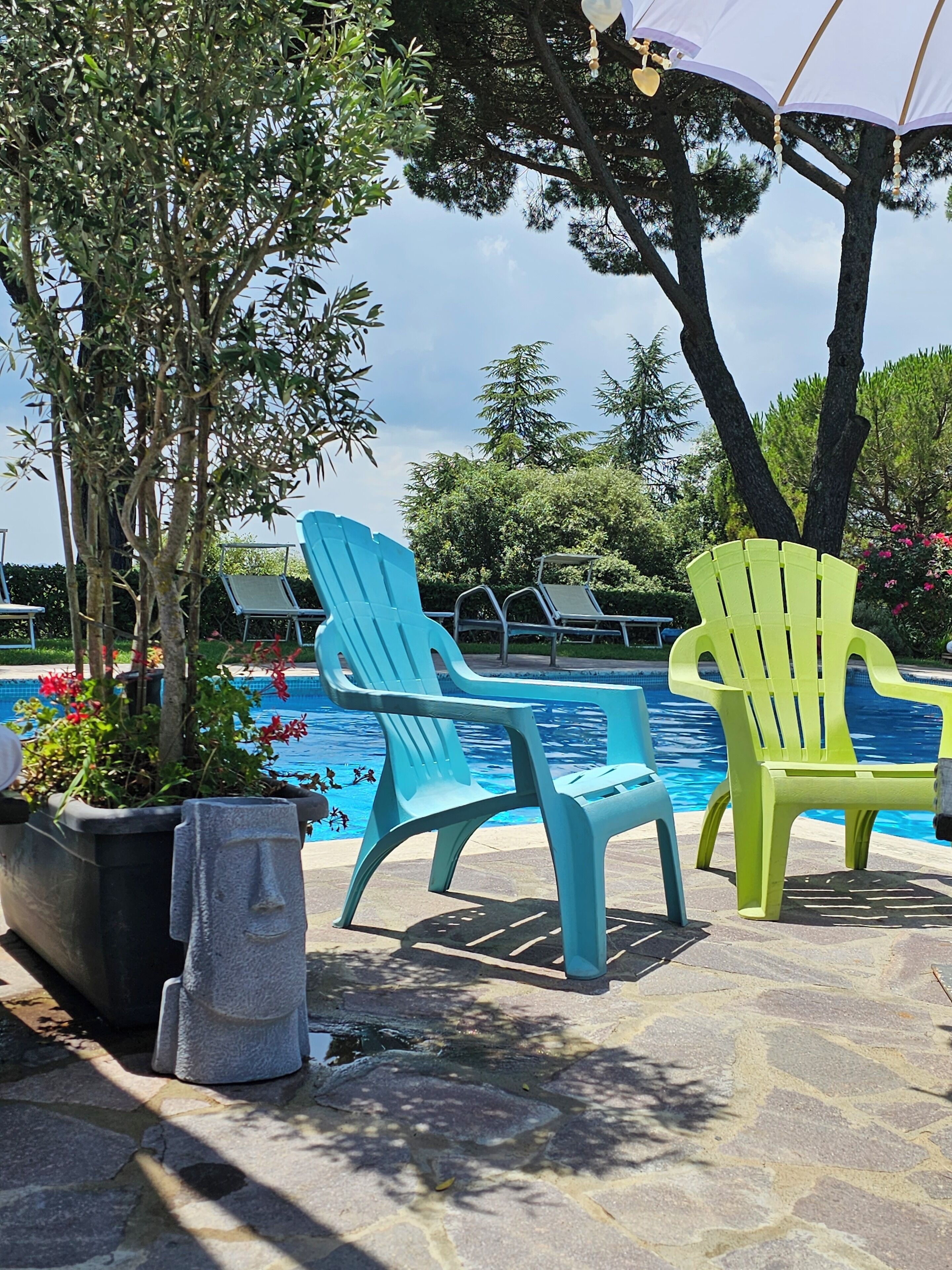 Zona junto a la piscina con dos sillas, un sendero de piedra y un árbol grande.