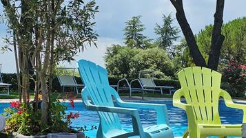 Zona junto a la piscina con dos sillas, un sendero de piedra y un árbol grande.