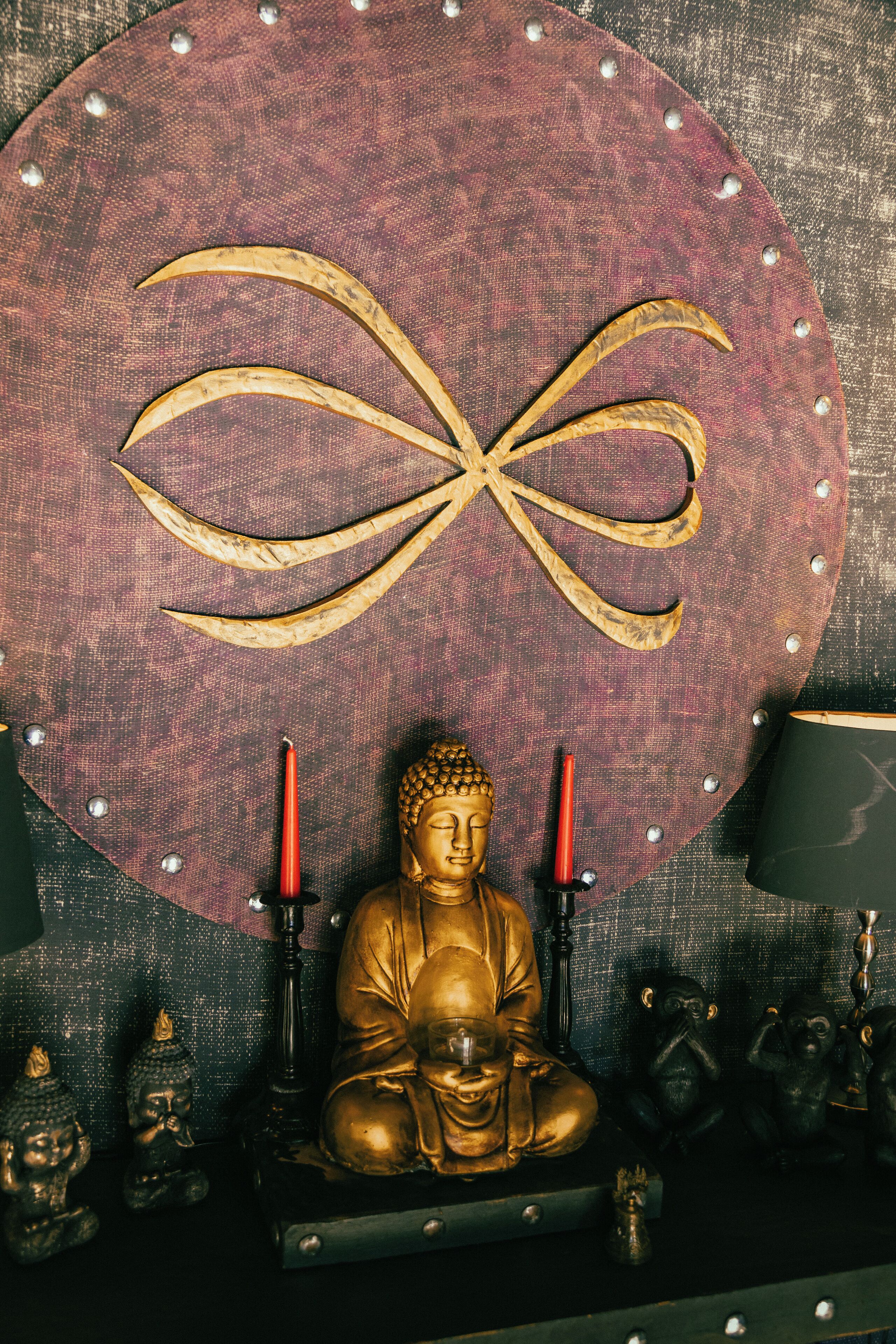 Eine Buddha-Statue mit zwei Kerzen, umgeben von kleinen Figuren auf einem Regal.