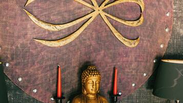 Eine Buddha-Statue mit zwei Kerzen, umgeben von kleinen Figuren auf einem Regal.