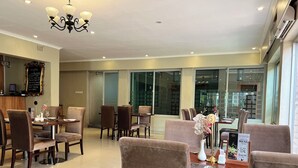 A dining area with a chandelier, a menu stand, and a view of the outside through large windows. - Lotus by Serendib (Blantyre)