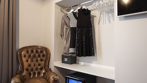 Una habitación con una butaca de cuero marrón, una estantería con ropa, un televisor y una consola de videojuegos.