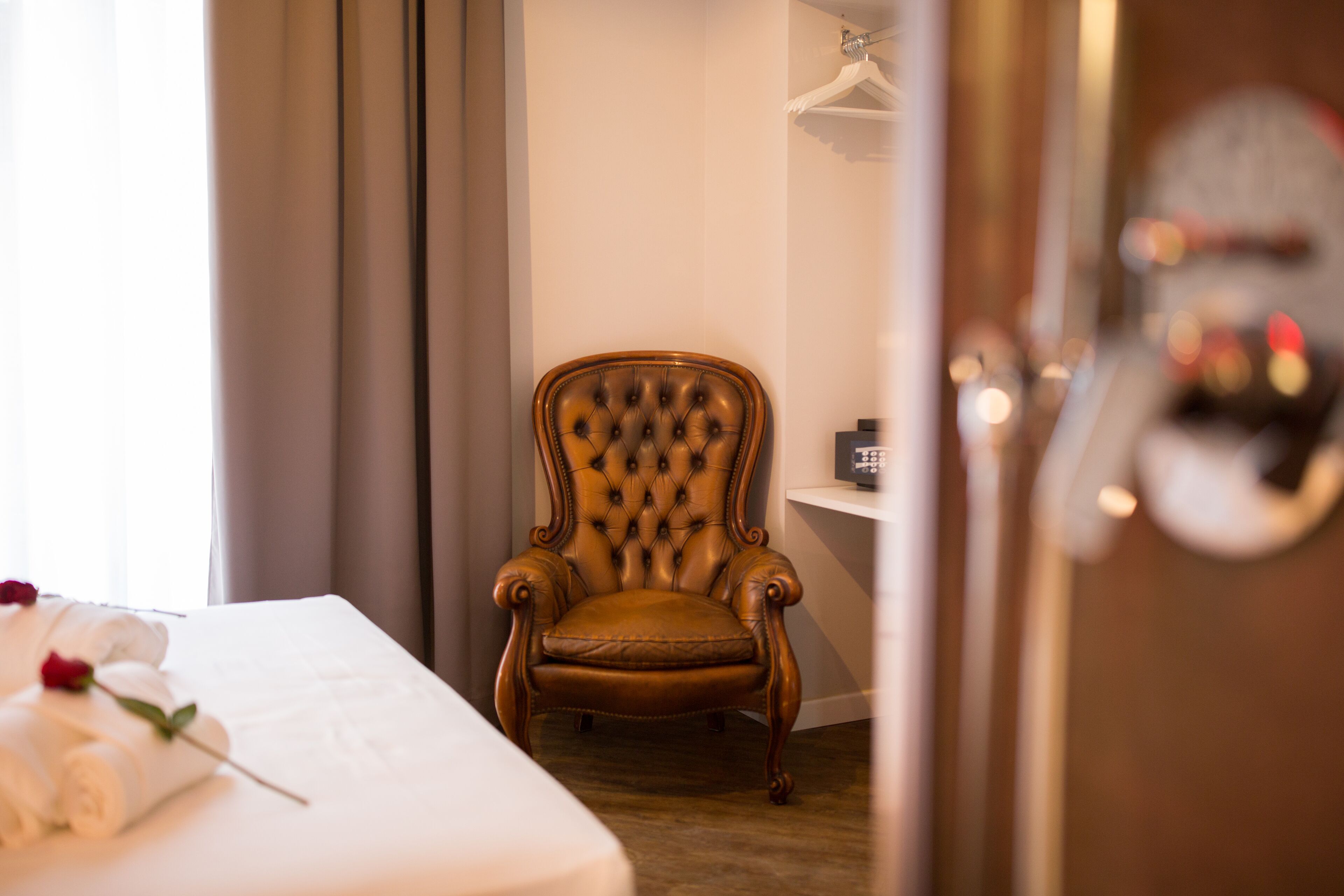 A hotel room with a bed, a tufted leather armchair, a bedside table, and a wardrobe.