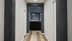 Un pasillo con piso de madera, paredes oscuras y una cocina visible a través de una puerta.