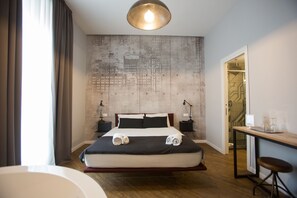 A modern hotel room with a large bed, a desk with a chair, and a view of the cityscape through the window. - Ara Suite (Rome)