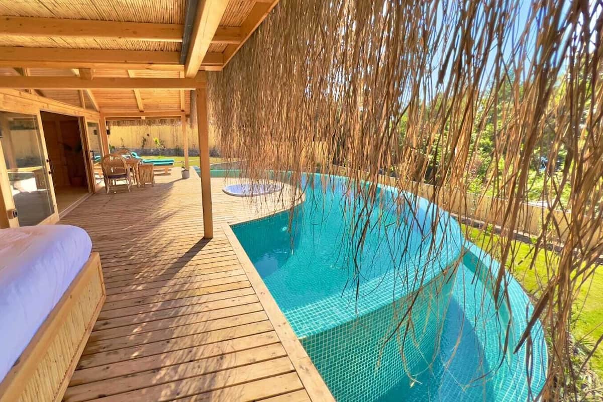 A wooden deck with a pool, a bed, and a dining area.